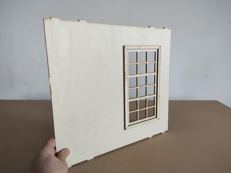 May include: A flat, rectangular light-colored wooden panel featuring a cutout window frame with a grid pattern. The panel has small tabs along the top and bottom edges, indicating it is a component designed for assembly into a larger structure.