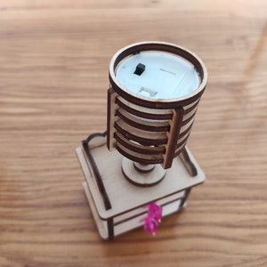 May include: A wooden model of a lamp with a white base and a brown wooden shade. The lamp has a small black switch on the side.