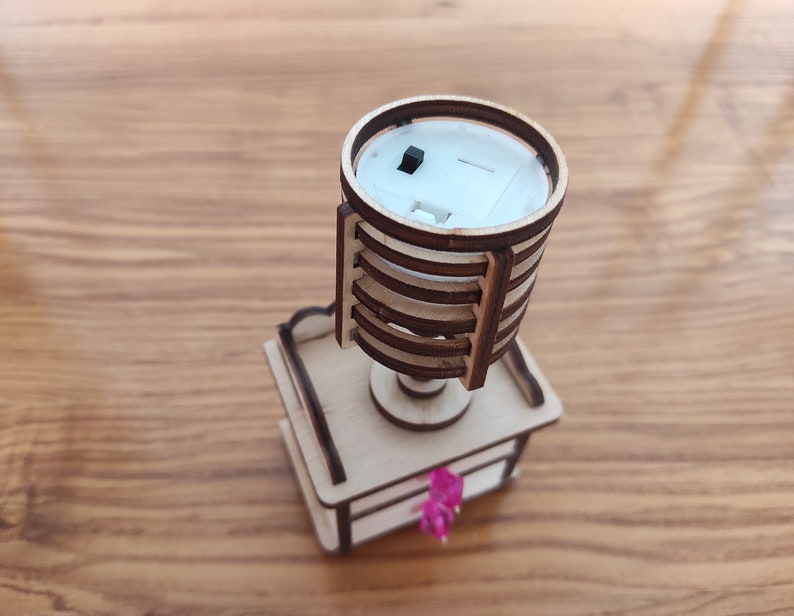 May include: A wooden model of a lamp with a white base and a brown wooden shade. The lamp has a small black switch on the side.