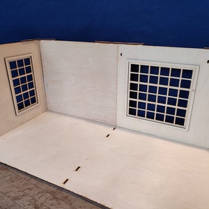 May include: A wooden model room with two windows, each with a grid pattern. The room is unfinished and has a light wood finish.