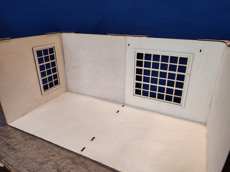 May include: A wooden model room with two windows, each with a grid pattern. The room is unfinished and has a light wood finish.