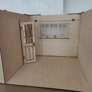 May include: A miniature wooden dollhouse room with a white door, a window with a white frame, and a light wood floor.