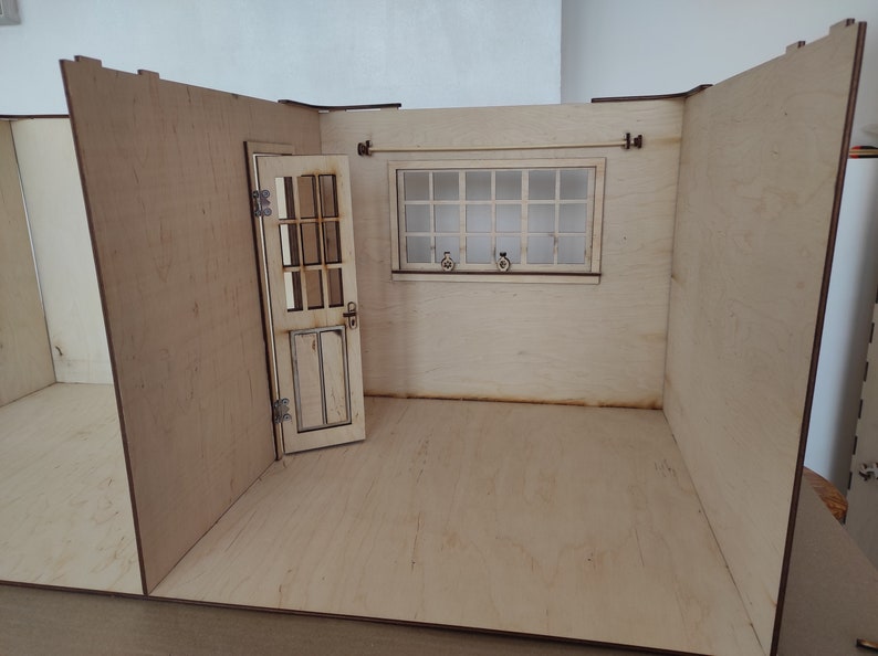 May include: A miniature wooden dollhouse room with a white door, a window with a white frame, and a light wood floor.