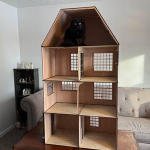 以下が含まれることがあります： 木製の人形の家で、黒い猫が最上階に座っています。人形の家には、窓とドアのある部屋がいくつかあります。