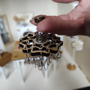 May include: A wooden chandelier with a black and brown mandala design and crystal accents. The chandelier is hanging from a silver chain.