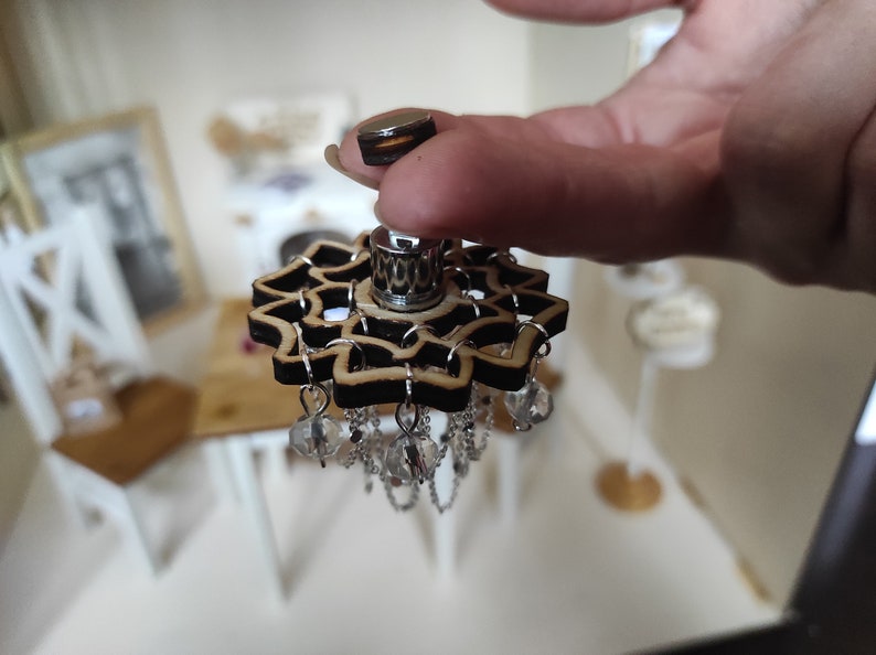 May include: A wooden chandelier with a black and brown mandala design and crystal accents. The chandelier is hanging from a silver chain.