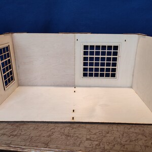 May include: A white wooden dollhouse room with two windows, one with a grid pattern and the other with a simple frame. The room has a white wooden floor and is ready for decorating.