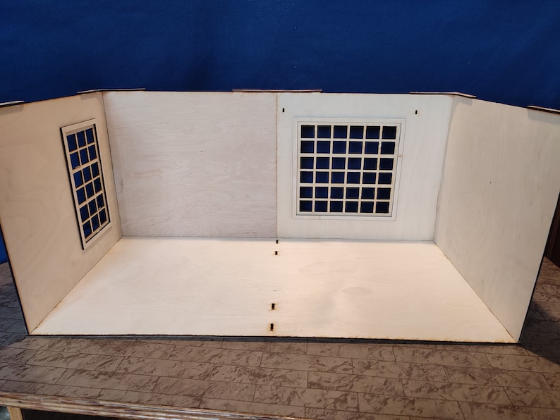 May include: A white wooden dollhouse room with two windows, one with a grid pattern and the other with a simple frame. The room has a white wooden floor and is ready for decorating.