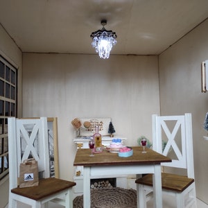 May include: A miniature dollhouse dining room with a white table and chairs, a small chandelier, a bottle of wine, a cake, and a Christmas tree. The room is decorated with a sign that says "Wishing you a Merry Christmas and a Happy New Year".