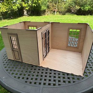 Puede incluir: Un modelo de casa de muñecas de madera con dos habitaciones, una con una puerta y la otra con una ventana. La casa de muñecas está hecha de madera contrachapada y tiene un acabado de madera natural.