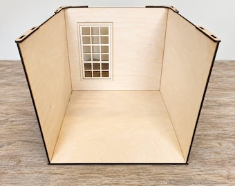 Könnte beinhalten: Eine Puppenhaus-Raumstruktur aus hellem Holz mit drei Wänden und einem Boden. Die Rückwand enthält einen einzelnen rechteckigen Fensterrahmen mit Gittermuster. Die Kanten der Holzplatten sind dunkel und zeigen lasergeschnittene Verbindungen.