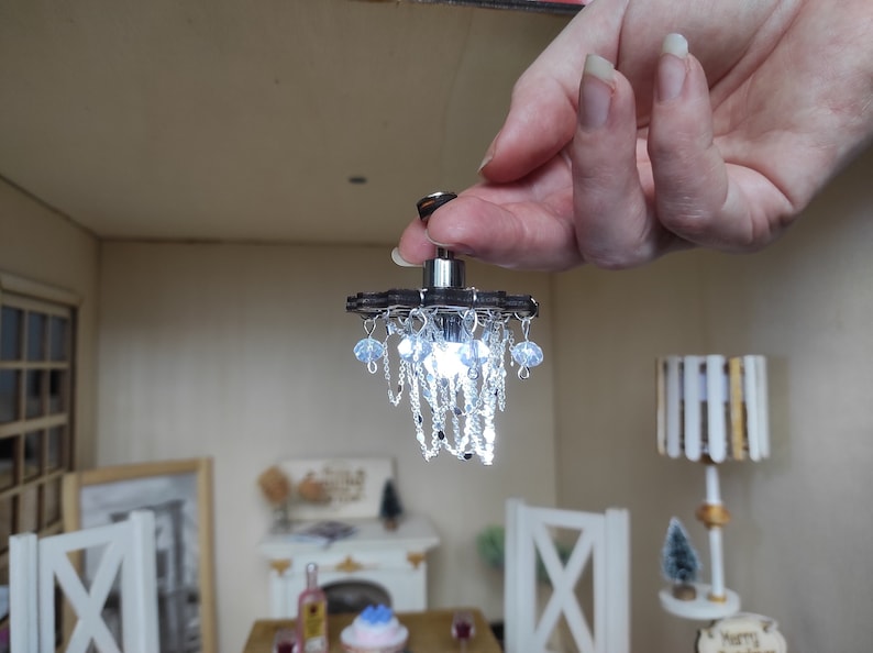 May include: A miniature chandelier with a brown wooden base and clear crystal accents. The chandelier has a single white light bulb and is hanging from a silver chain.