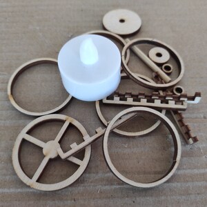 May include: A white LED tea light candle sits on top of a pile of wooden craft pieces, including circles, a gear, and a decorative strip.