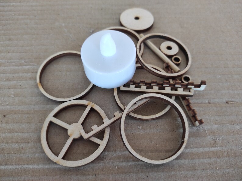 May include: A white LED tea light candle sits on top of a pile of wooden craft pieces, including circles, a gear, and a decorative strip.