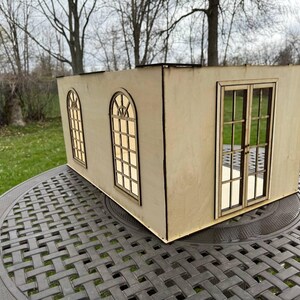 Puede incluir: Un modelo de madera de un peque&ntilde;o edificio con tres ventanas y una puerta doble. El modelo est&aacute; hecho de madera marr&oacute;n claro y tiene un dise&ntilde;o simple.