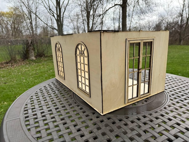 Puede incluir: Un modelo de madera de un peque&ntilde;o edificio con tres ventanas y una puerta doble. El modelo est&aacute; hecho de madera marr&oacute;n claro y tiene un dise&ntilde;o simple.