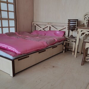 May include: A wooden dollhouse bedroom set with a pink bed, a wooden nightstand, and a vanity with a mirror. The bed has a pink satin comforter and a wooden headboard.