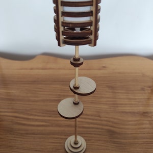 May include: A wooden floor lamp with a cylindrical shade made of stacked wooden rings. The lamp has two round shelves and a base made of stacked wooden circles.