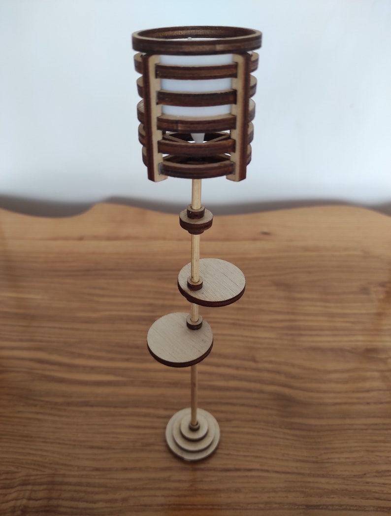 May include: A wooden floor lamp with a cylindrical shade made of stacked wooden rings. The lamp has two round shelves and a base made of stacked wooden circles.