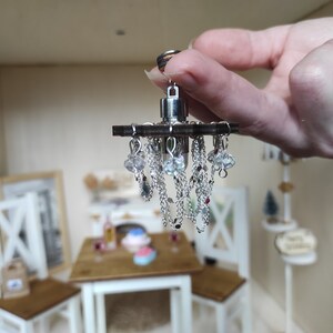 May include: A miniature silver chandelier with crystal beads and chains hanging from a wooden base.