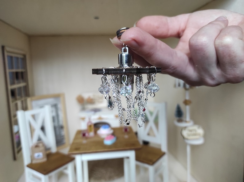 May include: A miniature silver chandelier with crystal beads and chains hanging from a wooden base.
