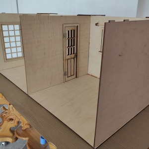 May include: A wooden dollhouse room kit with walls, a door, and a window. The room is unfinished and ready to be assembled.