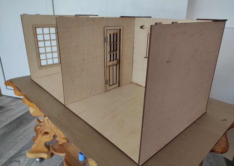 May include: A wooden dollhouse room kit with walls, a door, and a window. The room is unfinished and ready to be assembled.
