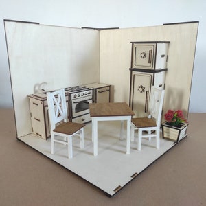 Könnte beinhalten: Eine Miniatur-Holzküche mit Herd, Kühlschrank, Tisch, Stühlen und einem Blumenkasten. Die Möbel sind weiß und braun lackiert und weisen filigrane Details auf. Das Set wird in einer Ecke präsentiert.