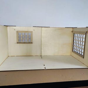 May include: A light-colored wooden dollhouse room structure featuring three walls and a floor. The back wall includes a small square window with a grid pattern, while the right side wall features a larger rectangular window with a grid design.