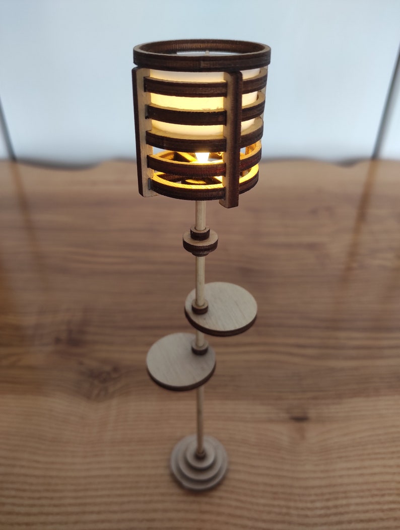 May include: A wooden floor lamp with a cylindrical shade made of thin wooden slats. The lamp has a warm, white light and a simple, modern design.