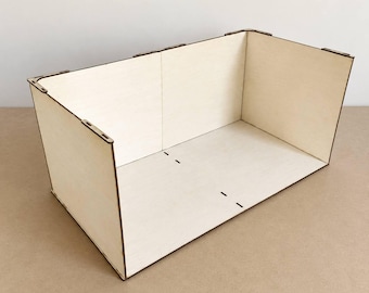 May include: A rectangular open-top box constructed from light-colored plywood panels. The structure features visible interlocking joints at the corners and edges, with dark brown laser-cut edges contrasting against the pale wood surfaces.