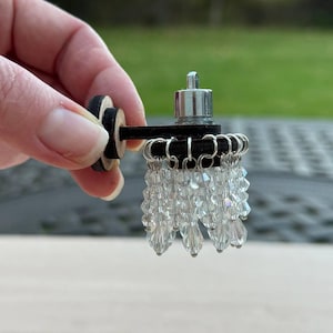 Peut inclure: Un lustre miniature avec une base en bois noir et une chaîne argentée avec des perles de cristal.