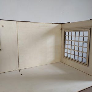 May include: A light-colored wooden dollhouse room structure featuring two walls and a floor. The left wall has a small window with six panes, while the right wall contains a larger window with a grid of thirty-five square panes. The wood is smooth.
