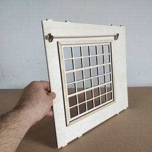 May include: A white wooden window frame with a grid of small squares. The window has a wooden dowel rod across the top.