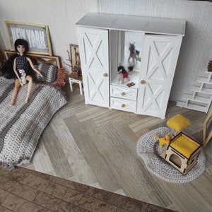 May include: A miniature dollhouse bedroom set featuring a bed with a gray and white striped crocheted blanket, a white wooden wardrobe with X-patterned doors, a small side table, a white tiered shelf, a round gray rug, and a yellow cat-themed pet house.
