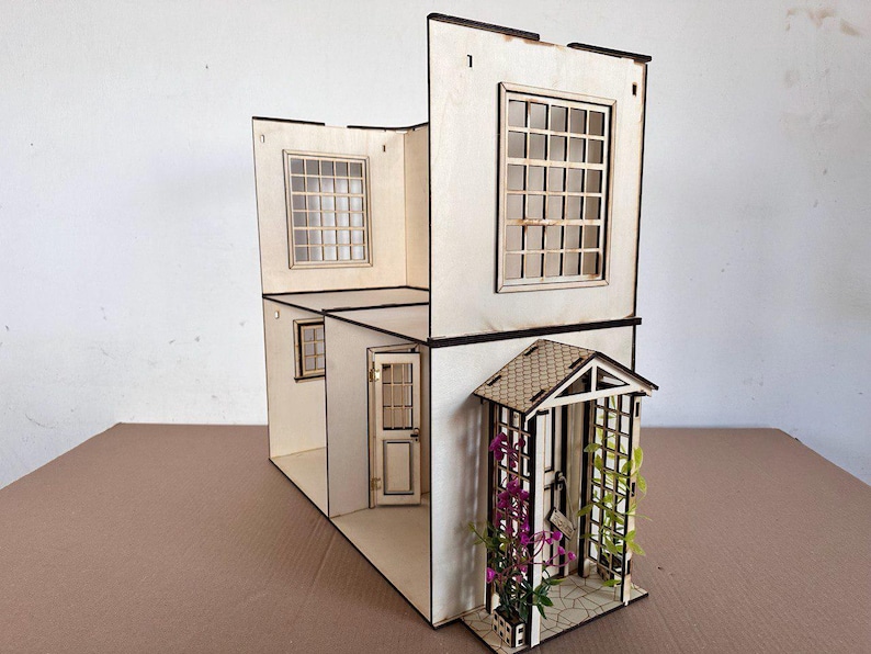 May include: A two-story wooden dollhouse structure with light-colored walls, multiple grid-patterned windows, and a front door. The exterior features a small porch with a peaked roof, a trellis, and artificial purple and green climbing plants.