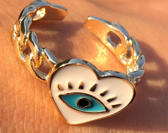 Puede incluir: Anillo de oro con un dije de corazón blanco con un diseño de ojo azul malvado. El anillo está hecho de una banda de estilo cadena.