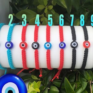 Könnte beinhalten: Zehn bunte Armbänder aus Kordel mit einem bösen Blick-Anhänger. Die Armbänder sind auf einer weißen Oberfläche mit den Zahlen 1 bis 10 darüber angeordnet. Die bösen Blick-Anhänger sind blau, rot und schwarz.