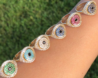 Puede incluir: Siete anillos de oro con un diseño de ojo turco azul, turquesa, negro, verde y rojo. Cada anillo está adornado con diamantes de imitación transparentes.