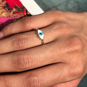 May include: A gold ring with a white enamel evil eye design. The eye is blue.