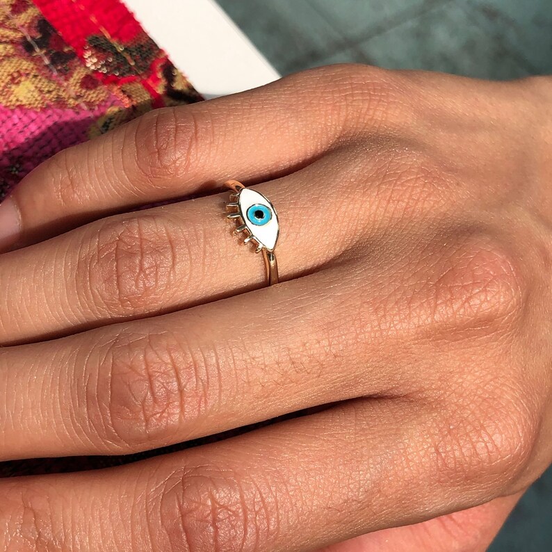 May include: A gold ring with a white enamel evil eye design. The eye is blue.