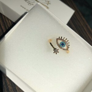 May include: Gold ring with a blue evil eye design and clear rhinestones. The ring is open and adjustable.