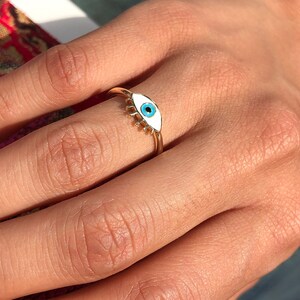 May include: Gold ring with a white enamel evil eye design. The eye is blue.