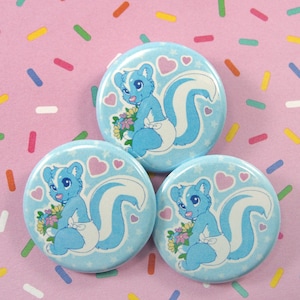 May include: Three blue and white button pins with a cartoon skunk wearing a diaper and holding flowers. The background is a pink and white confetti pattern.