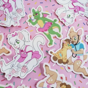 May include: A collection of colorful stickers featuring various cartoon animals wearing pink dresses and diapers. The stickers are on a pink background with white sprinkles.