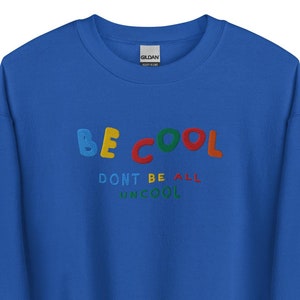 Puede incluir: Una sudadera azul real con el texto "BE COOL DON'T BE ALL UNCOOL" en letras bordadas de colores.