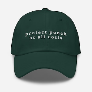 以下が含まれることがあります： 白い文字で「protect punch at all costs」と刺繍された濃い緑色の野球帽。 つばがカーブしており、上部にボタンが付いています。 クラシックでカジュアルなアクセサリーです。
