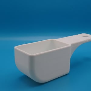 May include: A white plastic measuring scoop with a handle. The scoop is rectangular and has a rounded bottom.
