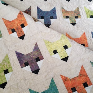 May include: A quilt with a pattern of fox faces in various colors and patterns. The quilt is made with a white background and the fox faces are made with different fabrics.