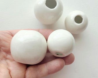 May include: Four white ceramic spheres with a hole in the center. The spheres are different sizes and are arranged on a white surface.